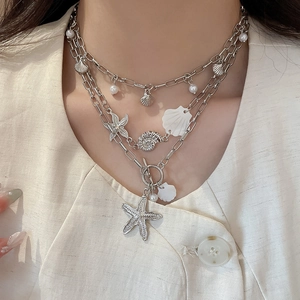 Macro detail of multilayer silver necklace with starfish, shell charms and pearls