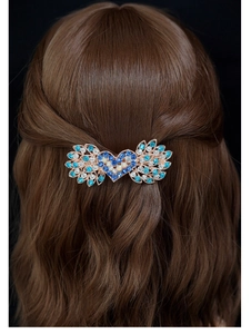 Dettaglio di un fermaglio a cuore alato con strass blu su capelli castani ricci