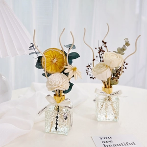 Detail of two reed diffusers with dried flowers in square textured glass bottles
