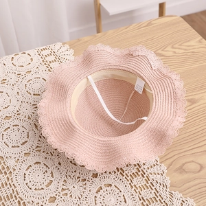 Détail d'un chapeau de paille rose avec bord ondulé et cordon sur tapis en dentelle