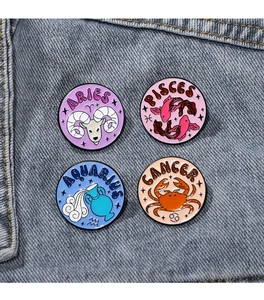 Detail of four colorful enamel zodiac pins including Aries and Pisces on denim fabric
