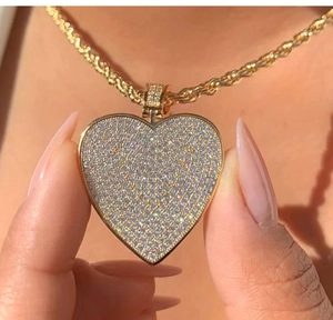Close-up of a large iced-out heart pendant necklace with gold rope chain on person