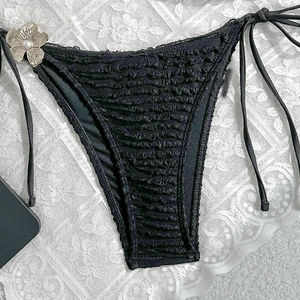 Detail of black ruffled bikini bottoms with side ties and pearl floral metal charm