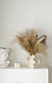 Artistic detail of a white shell-shaped ceramic vase with dried reed in a Nordic setup