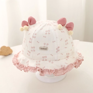Détail du chapeau bébé avec imprimés cerises, nœuds roses et pompons doux