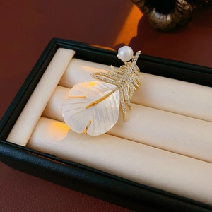 Macro detail of gold-plated feather brooch with zircon, pearl, and white mother-of-pearl inlay