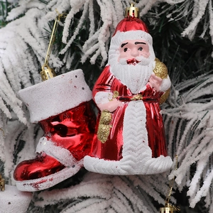 Festive Santa and red boots ornaments with glitter hanging on a snowy Christmas tree branch