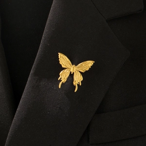 Detail view of a golden butterfly brooch with metallic texture on a black blazer lapel