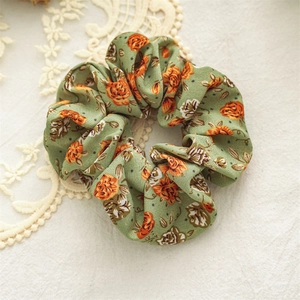 Detailed close-up of floral scrunchie with orange rose pattern on green fabric