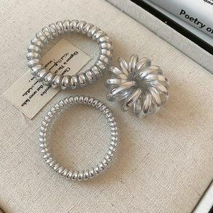 Close-up of three silver spiral hair ties set against a textured aesthetic background