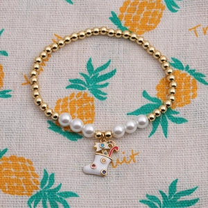 Gros plan d'un bracelet de Noël doré orné de perles blanches et d'un pendentif chaussette