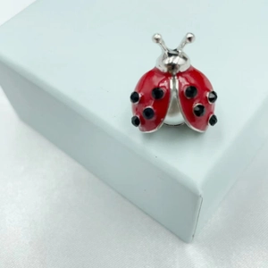 Detail of ladybug brooch featuring red enamel, black crystals and a large pearl base
