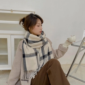 Beige cashmere-like scarf with black plaid patterns and fringe worn by a female model