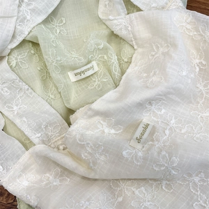Detailed close-up of Szakka embroidered fabric with white floral patterns and soft texture