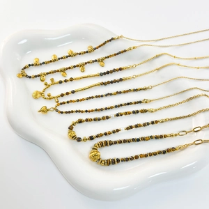 Detail of natural tiger eye beaded necklaces with gold charms on white ceramic tray