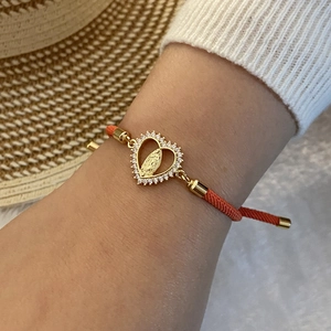 Close-up of red woven bracelet featuring a gold Madonna heart pendant with crystals