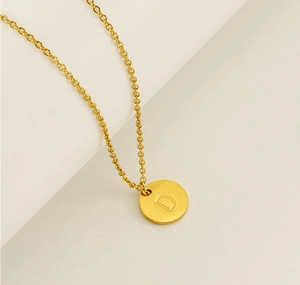 Détail d'un collier en acier inoxydable doré avec pendentif rond et gravure de la lettre D