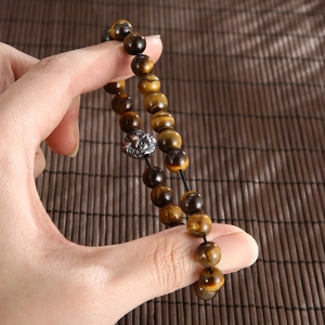 Handheld tiger eye stone bead bracelet with a metallic lion head charm and elastic cord