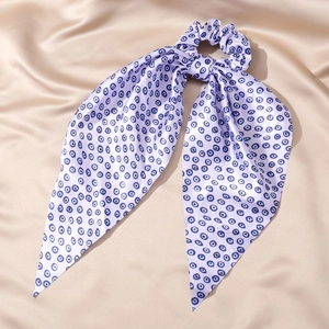 Detail view of a lavender satin scrunchie with blue evil eye prints and long ribbons