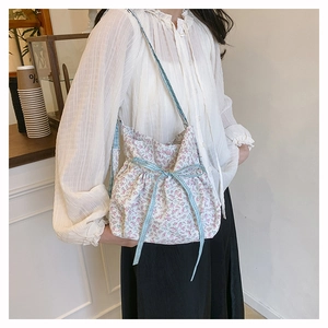 Detail of pink floral canvas tote bag with drawstring bow on a model's shoulder