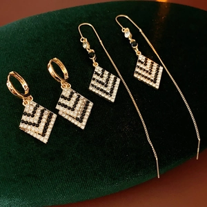 Detailansicht goldener Rauten-Ohrringe mit schwarzen und klaren Kristallen auf Samt
