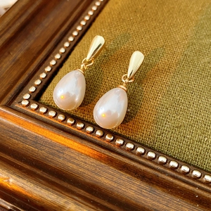 Detail of drop pearl earring with gold metal stud on vintage wood frame and green fabric