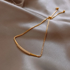 Macro detail of gold adjustable bracelet with zircon bar on champagne silk background