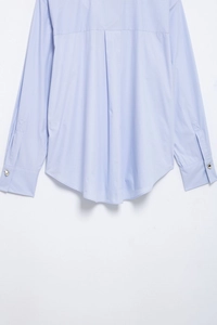Detail view of light blue striped shirt featuring a curved hem and button cuffs