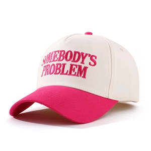 Detail of embroidered 'SOMEBODY'S PROBLEM' text on beige and pink baseball cap