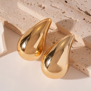Close-up of polished gold teardrop earrings displayed on a minimalist beige stone texture