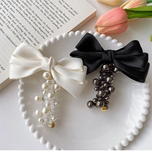 Detail of satin bow hair clips with faux pearls and elegant beads on decorative dish