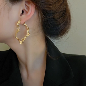 Macro side view of a model wearing a gold twisted heart-shaped earring with metallic luster