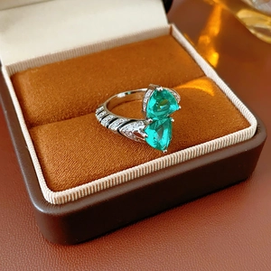 Detailed macro of silver ring with two heart green gemstones in velvet box