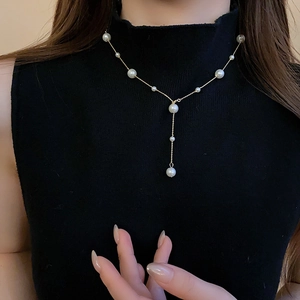 Detail of elegant Y-shaped pearl necklace on black sweater showing fine gold chain