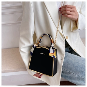 Detail of elegant black box bag featuring golden metal frame and silk scarf handle on model