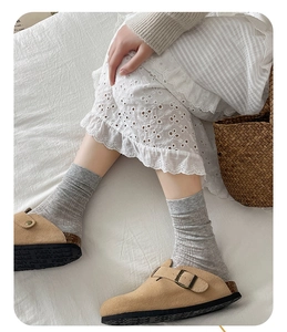 Detail of tan suede clogs featuring a metal buckle and cork sole on grey ribbed cotton socks