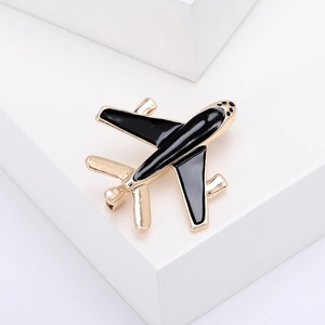 Macro detail of a gold and black enamel airplane brooch on a minimalist white stage