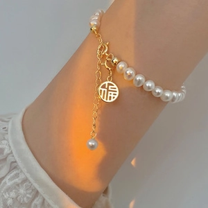 Detailansicht eines Perlenarmbands mit goldenem Fu-Anhänger am Handgelenk im Abendlicht