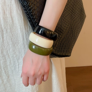 Gros plan sur un ensemble de bracelets en acrylique noir, crème et vert olive sur le poignet
