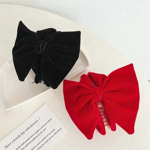 Detail of red and black velvet bow hair claws with pearl accents on a ceramic tray