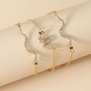 Detail of gold snake bracelets with white zircon pave and green stone eyes on a prop