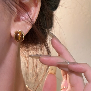 Close-up of vintage oval tiger eye stud earrings in 18k gold plating on an earlobe