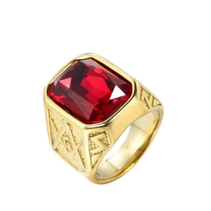Dettaglio di un anello massonico dorato con una grande pietra rossa su sfondo bianco