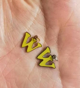Detailed macro view of yellow enamel letter W pendants held in hand for jewelry making