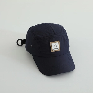 Detailed view of dark blue 5-panel cap with kindness smiley patch and metal eyelets