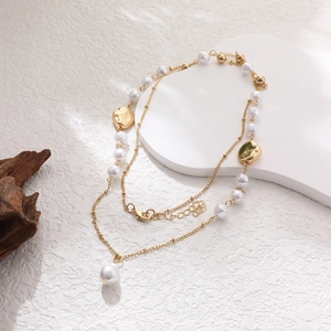 Double-layered 14K gold plated necklace with artificial pearls on a textured rock surface
