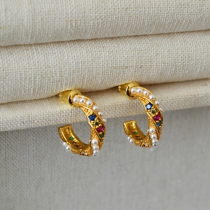 Close-up of gold twist earrings featuring inlaid pearls and multicolored zircon stones