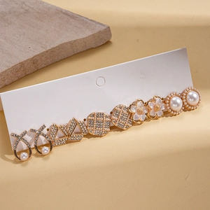 Detail of 10-piece gold flower earring set with pearls and rhinestones on stone background