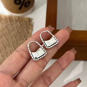 Macro detail of S925 sterling silver handbag-shaped earrings on a finger