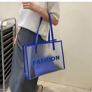 Detail of transparent PVC tote bag featuring blue trim and FASHION lettering text